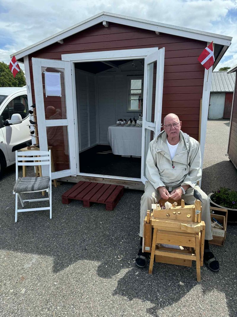 En sælger med sine varer foran en af de røde salgshytter